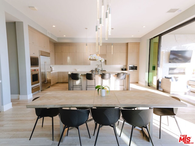 kitchen with a breakfast bar area, built in appliances, light brown cabinets, and a kitchen island