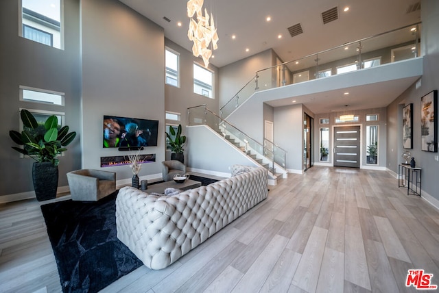 living room featuring a fireplace, a high ceiling, light hardwood / wood-style floors, and an inviting chandelier