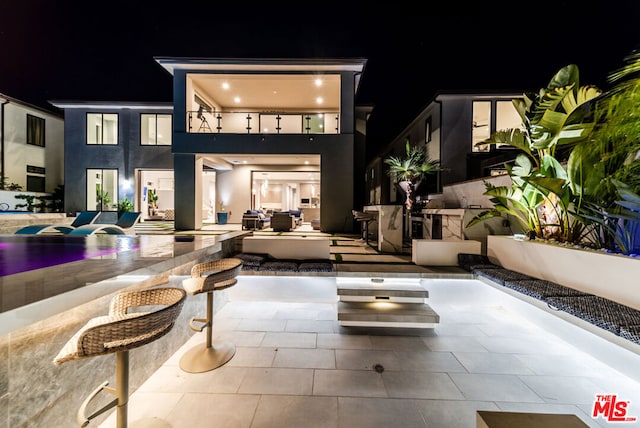 back house at twilight with an outdoor living space, a patio, and exterior kitchen