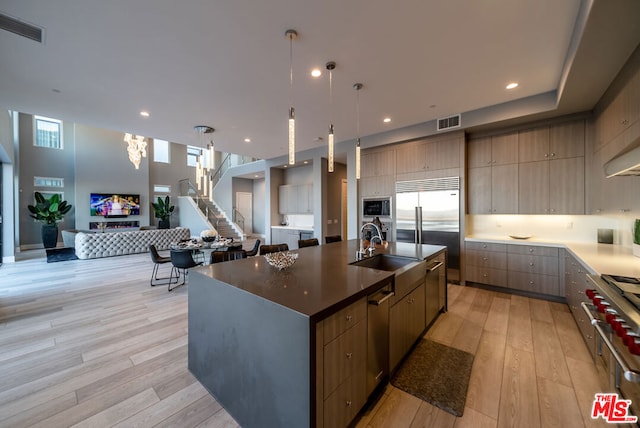 kitchen with light wood-type flooring, a spacious island, sink, pendant lighting, and built in appliances