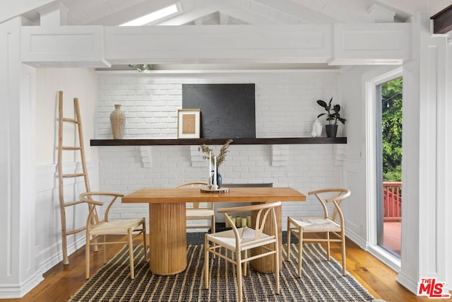 dining area with brick wall, wood-type flooring, and lofted ceiling with beams