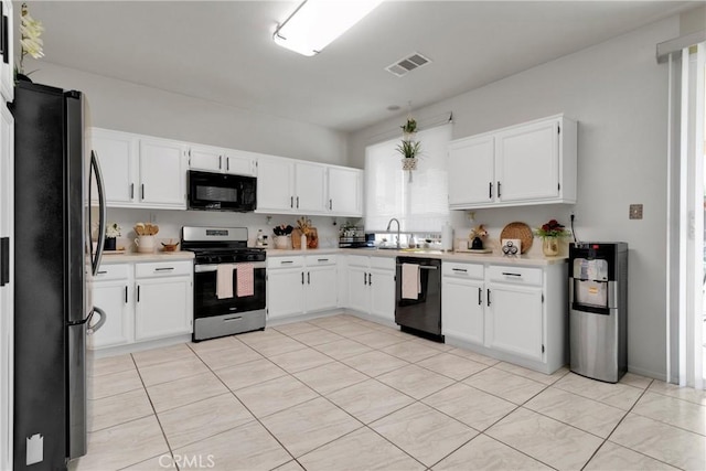 kitchen featuring white cabinetry, sink, water heater, light tile patterned floors, and black appliances