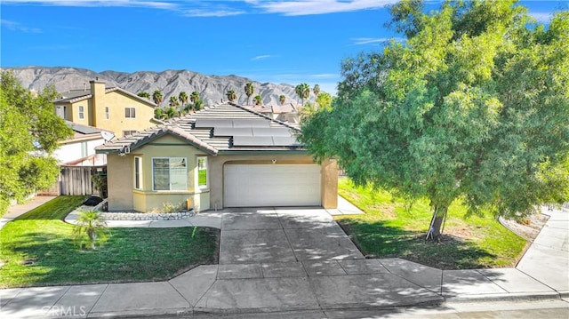 view of front of house featuring a mountain view, solar panels, a garage, and a front lawn