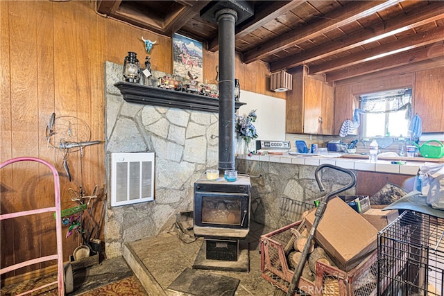 interior space featuring a wood stove, wood walls, beam ceiling, and wood ceiling