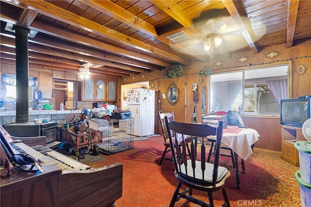 carpeted dining area with a wood stove, beamed ceiling, and wooden walls