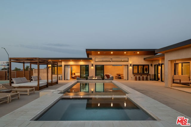 pool at dusk with an in ground hot tub and a patio area