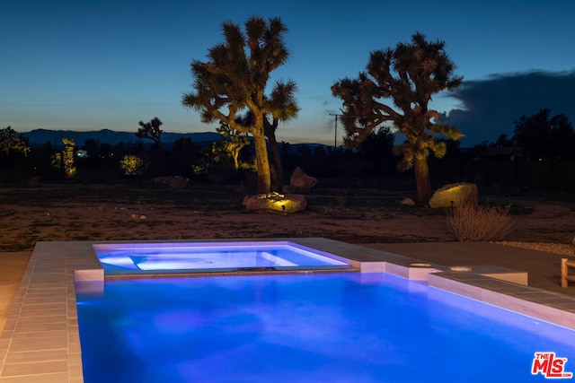 pool at dusk featuring an in ground hot tub and a mountain view