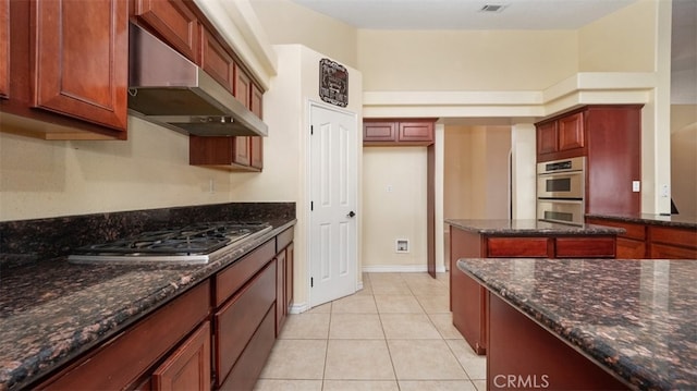 kitchen featuring stainless steel appliances, exhaust hood, dark stone counters, and light tile patterned floors