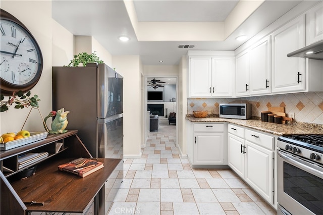 kitchen featuring appliances with stainless steel finishes, ceiling fan, dark stone counters, white cabinets, and decorative backsplash