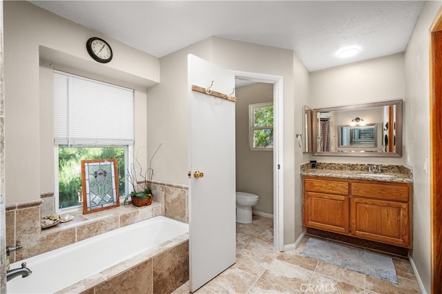 bathroom with vanity, a textured ceiling, toilet, and tiled tub