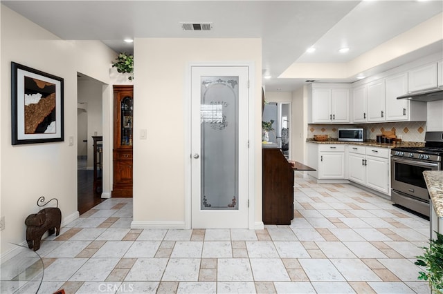 kitchen with stainless steel appliances, decorative backsplash, dark stone counters, and white cabinets