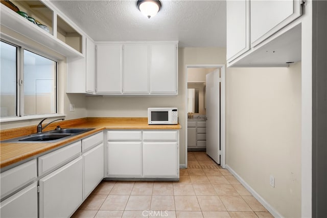 kitchen with light tile patterned flooring, a textured ceiling, sink, and white cabinets