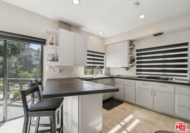 kitchen with a breakfast bar area, kitchen peninsula, white cabinets, and stainless steel gas cooktop