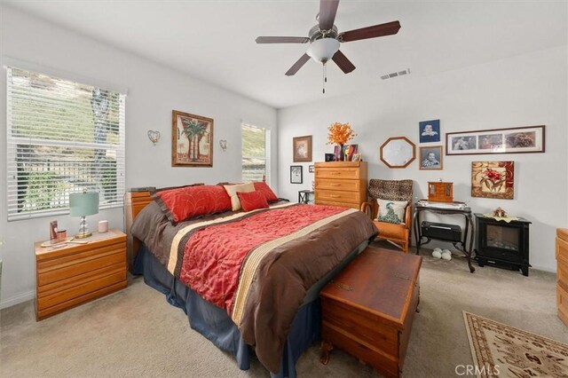 carpeted bedroom featuring ceiling fan, a wood stove, and multiple windows