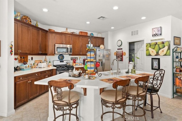 kitchen with a breakfast bar, stainless steel appliances, sink, light tile patterned floors, and an island with sink