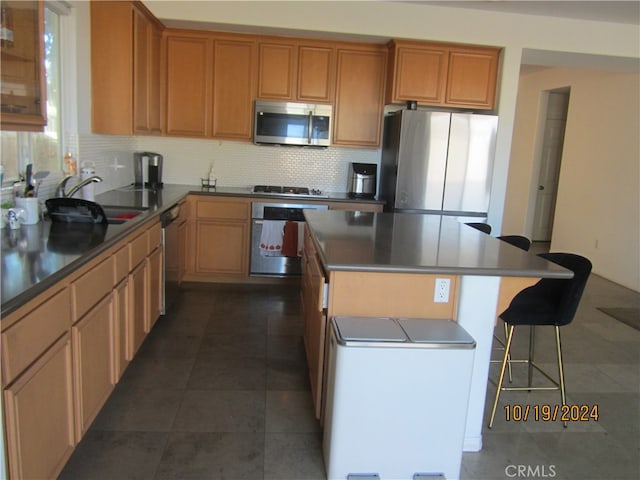 kitchen featuring sink, a kitchen island, backsplash, dark tile patterned floors, and stainless steel appliances