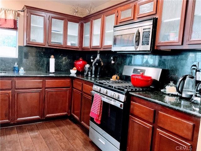 kitchen with decorative backsplash, stainless steel appliances, dark wood-type flooring, and dark stone countertops