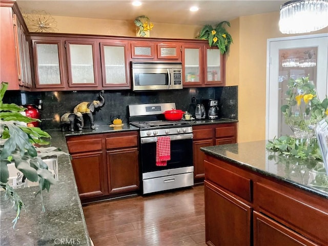 kitchen with appliances with stainless steel finishes, tasteful backsplash, dark hardwood / wood-style floors, and dark stone counters