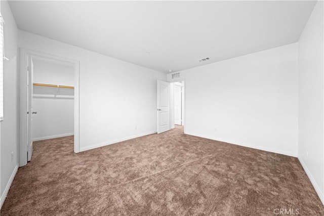 unfurnished bedroom featuring carpet flooring, a walk in closet, and a closet