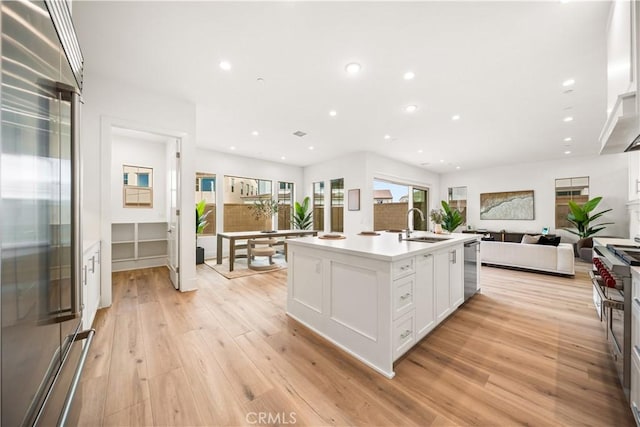 kitchen with white cabinetry, a center island with sink, light hardwood / wood-style floors, and premium appliances