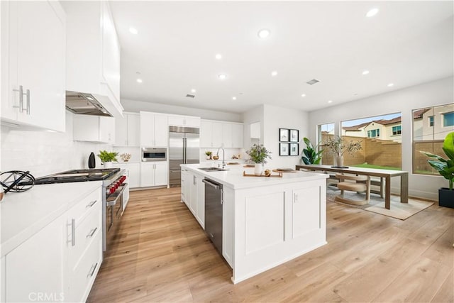 kitchen with a center island with sink, premium appliances, light hardwood / wood-style floors, and white cabinets