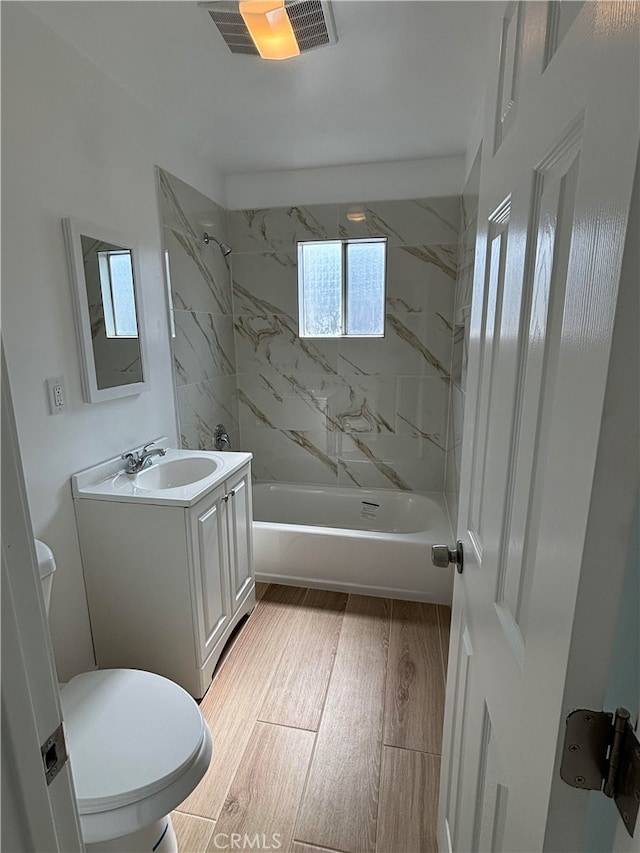 full bathroom featuring vanity, tiled shower / bath combo, wood-type flooring, and toilet