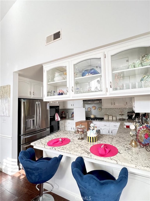 kitchen with white cabinetry, dark wood-type flooring, stainless steel refrigerator with ice dispenser, backsplash, and a breakfast bar