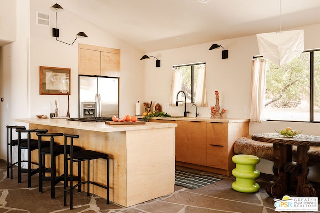 bar featuring lofted ceiling, sink, stainless steel fridge with ice dispenser, and light brown cabinets