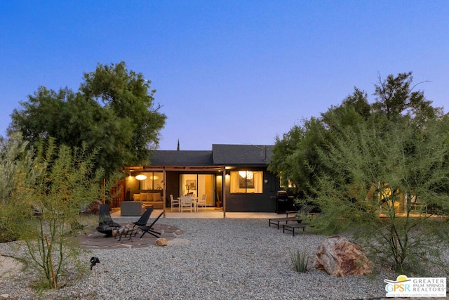 back house at dusk with an outdoor living space with a fire pit and a patio