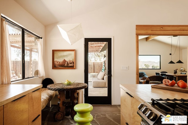 kitchen featuring lofted ceiling, stainless steel range with gas stovetop, light brown cabinets, and pendant lighting