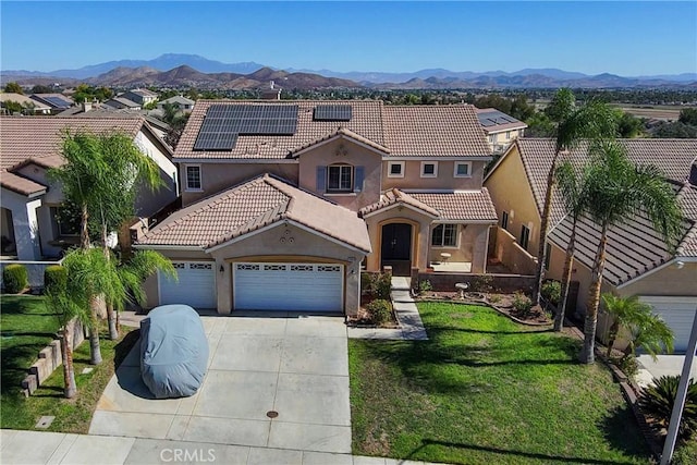 mediterranean / spanish house featuring a mountain view, solar panels, a garage, and a front yard