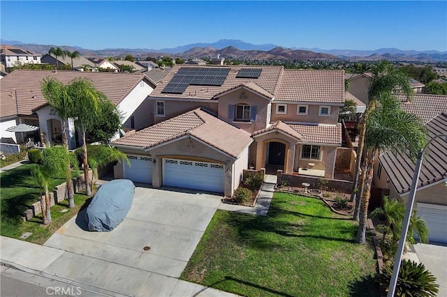 mediterranean / spanish house featuring a mountain view, solar panels, a garage, and a front lawn