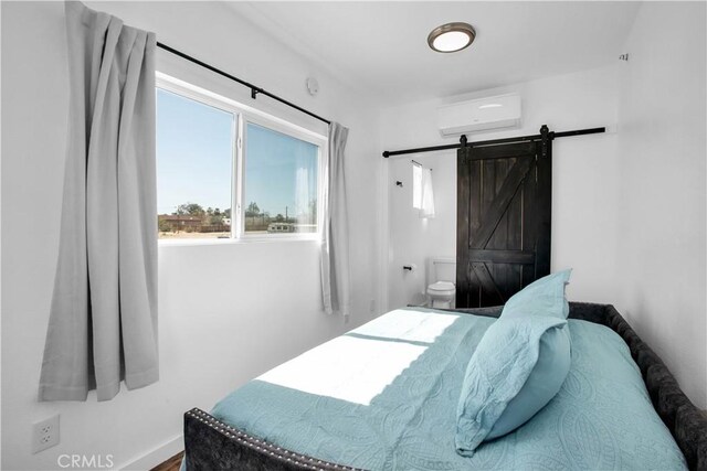 bedroom with wood-type flooring, a barn door, a wall unit AC, and ensuite bath