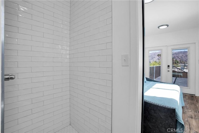 bathroom with hardwood / wood-style floors, a tile shower, and french doors