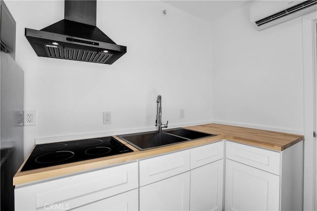 kitchen featuring black electric stovetop, an AC wall unit, sink, wall chimney exhaust hood, and white cabinetry