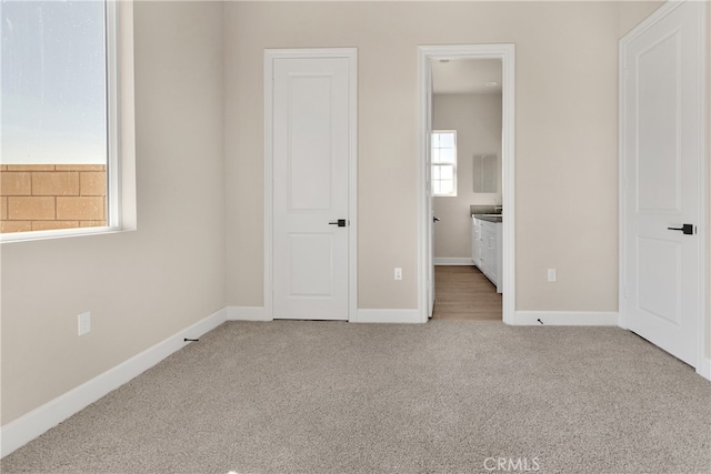 unfurnished bedroom with ensuite bathroom and light colored carpet