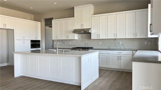 kitchen featuring white cabinetry, tasteful backsplash, stainless steel appliances, and a center island with sink