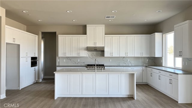 kitchen with light hardwood / wood-style floors, white cabinetry, a kitchen island with sink, and stainless steel oven