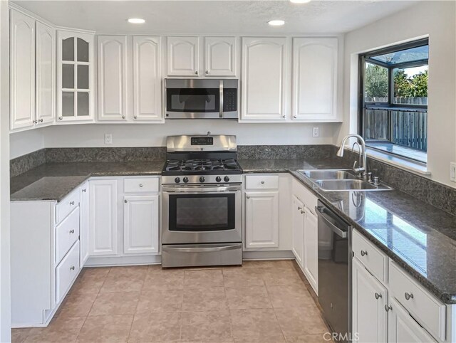 kitchen with appliances with stainless steel finishes, white cabinetry, dark stone countertops, and sink