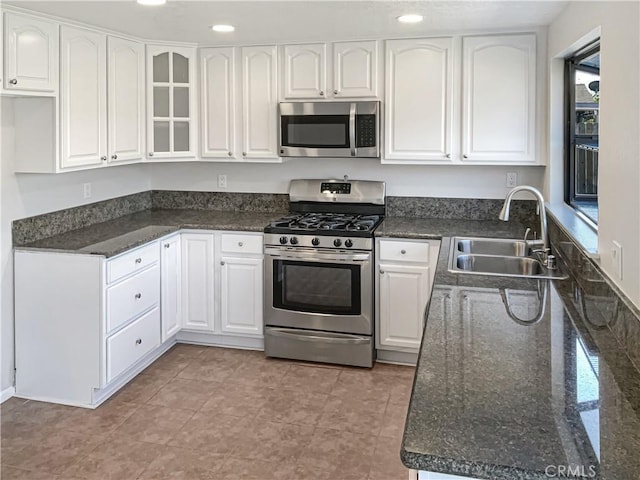 kitchen with white cabinetry, appliances with stainless steel finishes, sink, and dark stone counters