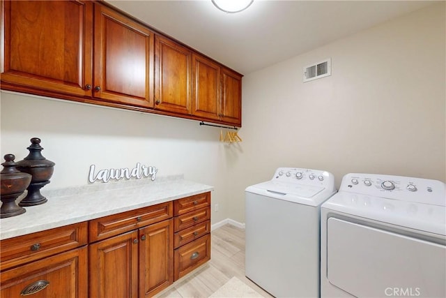 laundry room with washing machine and clothes dryer, light hardwood / wood-style flooring, and cabinets