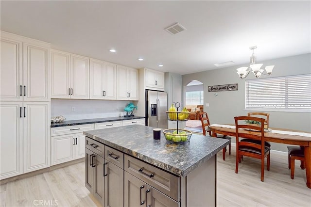 kitchen with a center island, stainless steel fridge, light wood-type flooring, decorative light fixtures, and white cabinetry