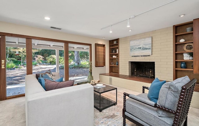 carpeted living room with a brick fireplace, rail lighting, and built in shelves