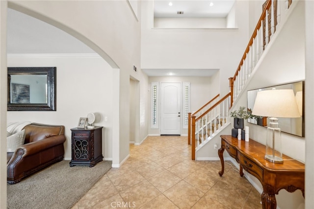 entrance foyer with tile patterned floors, ornamental molding, and a towering ceiling