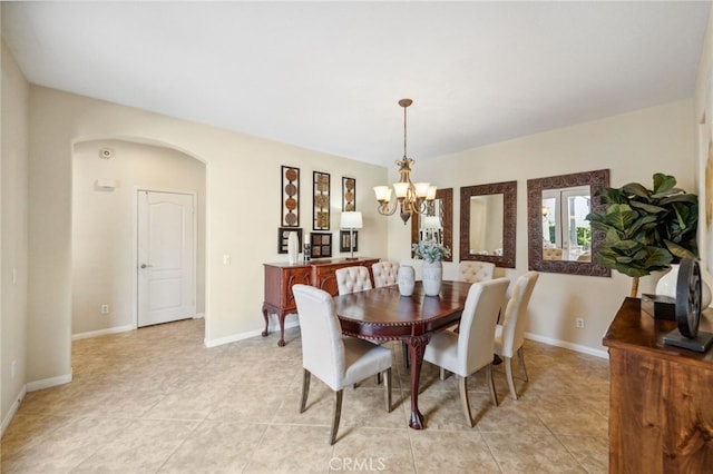 dining space featuring arched walkways, light tile patterned floors, a chandelier, and baseboards