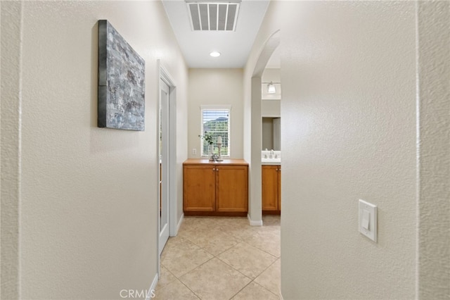 hallway with light tile patterned floors, baseboards, visible vents, and arched walkways