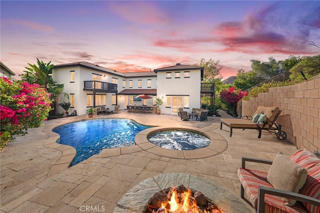 pool at dusk with a patio area, an outdoor fire pit, and an in ground hot tub