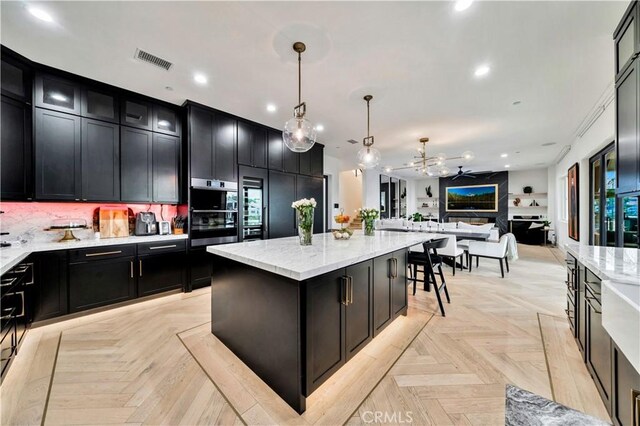 kitchen with visible vents, a ceiling fan, open floor plan, double oven, and dark cabinets