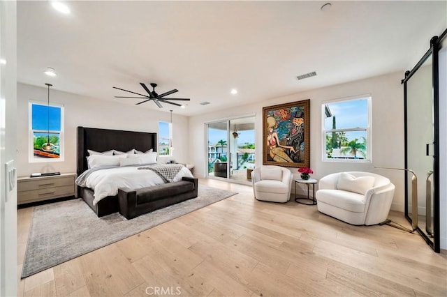 bedroom featuring light wood finished floors, multiple windows, a barn door, and access to outside