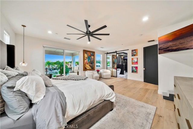 bedroom with light wood finished floors, visible vents, a barn door, recessed lighting, and access to outside